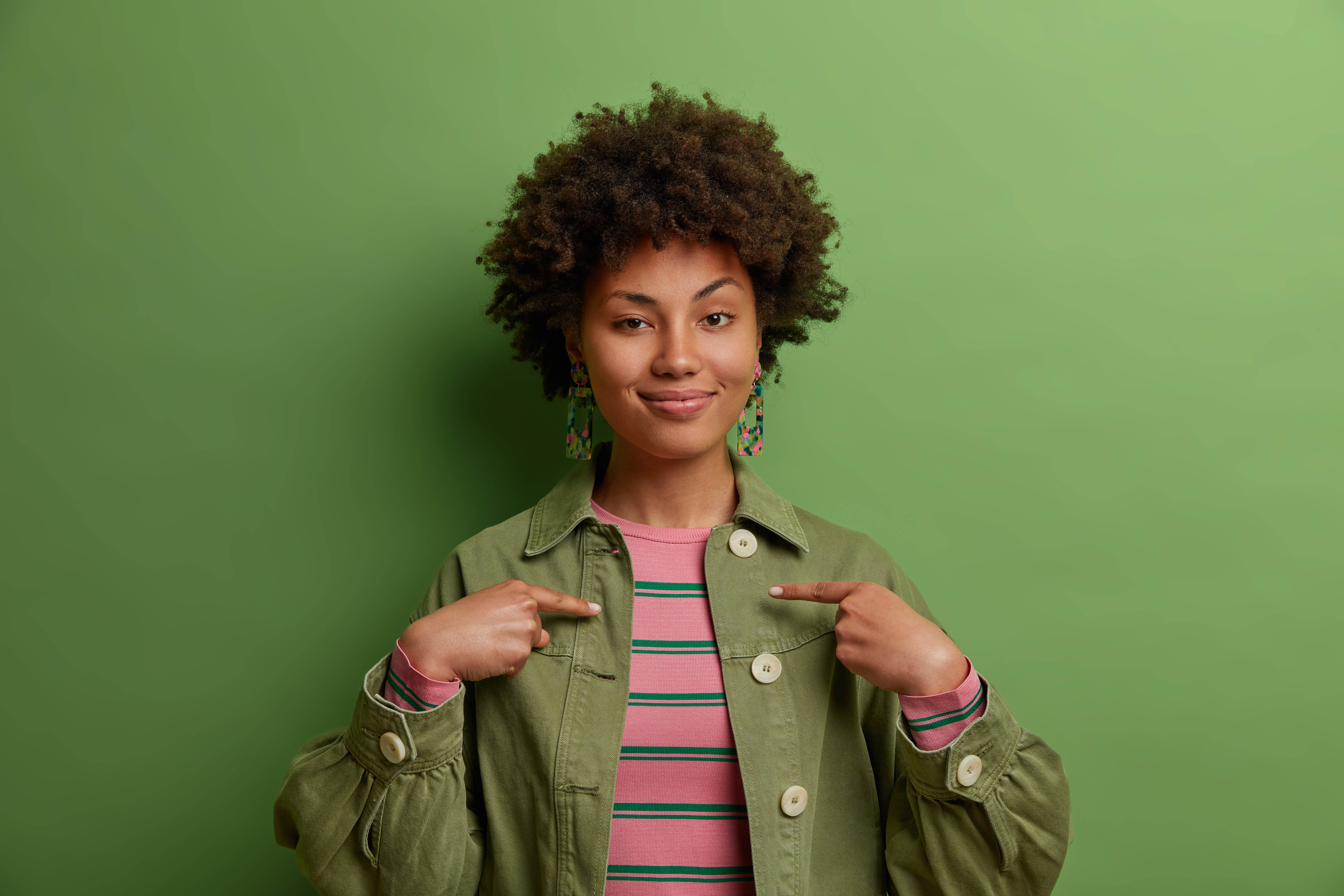 Young African American woman posing on a green background, facing the camera with her eyebrow raised Young African American woman posing on a green background, facing the camera with her eyebrow raised